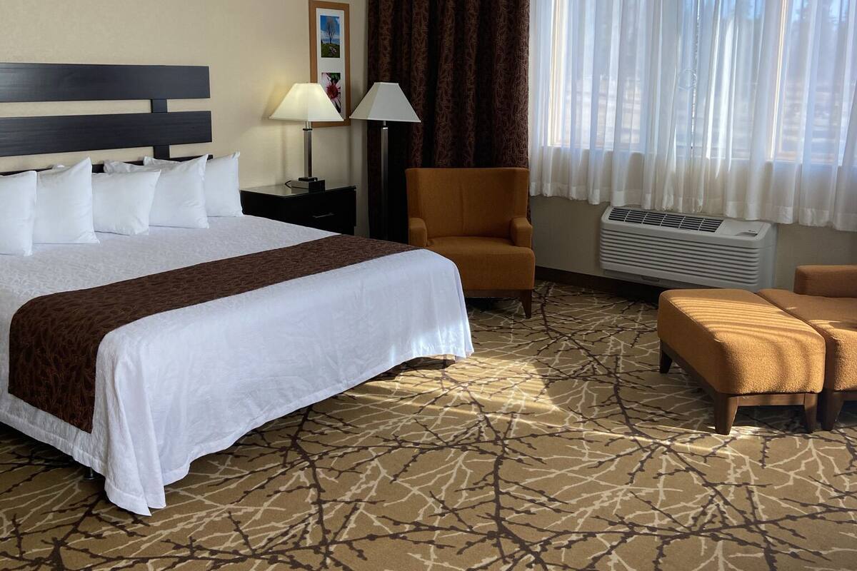 Een hotelkamer met een groot bed, een stoel, een tafel en een raam met gordijnen.