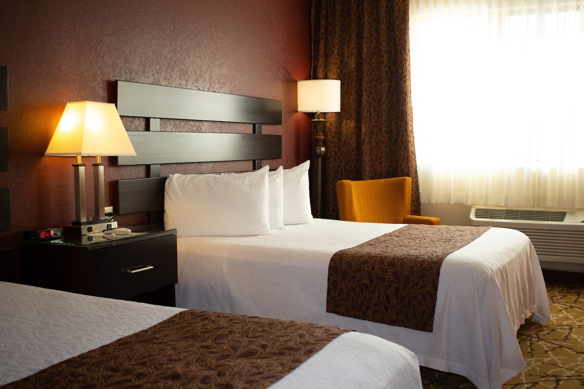 Een hotelkamer met twee bedden, een nachtkastje, een lamp, een stoel en een raam met gordijnen.
