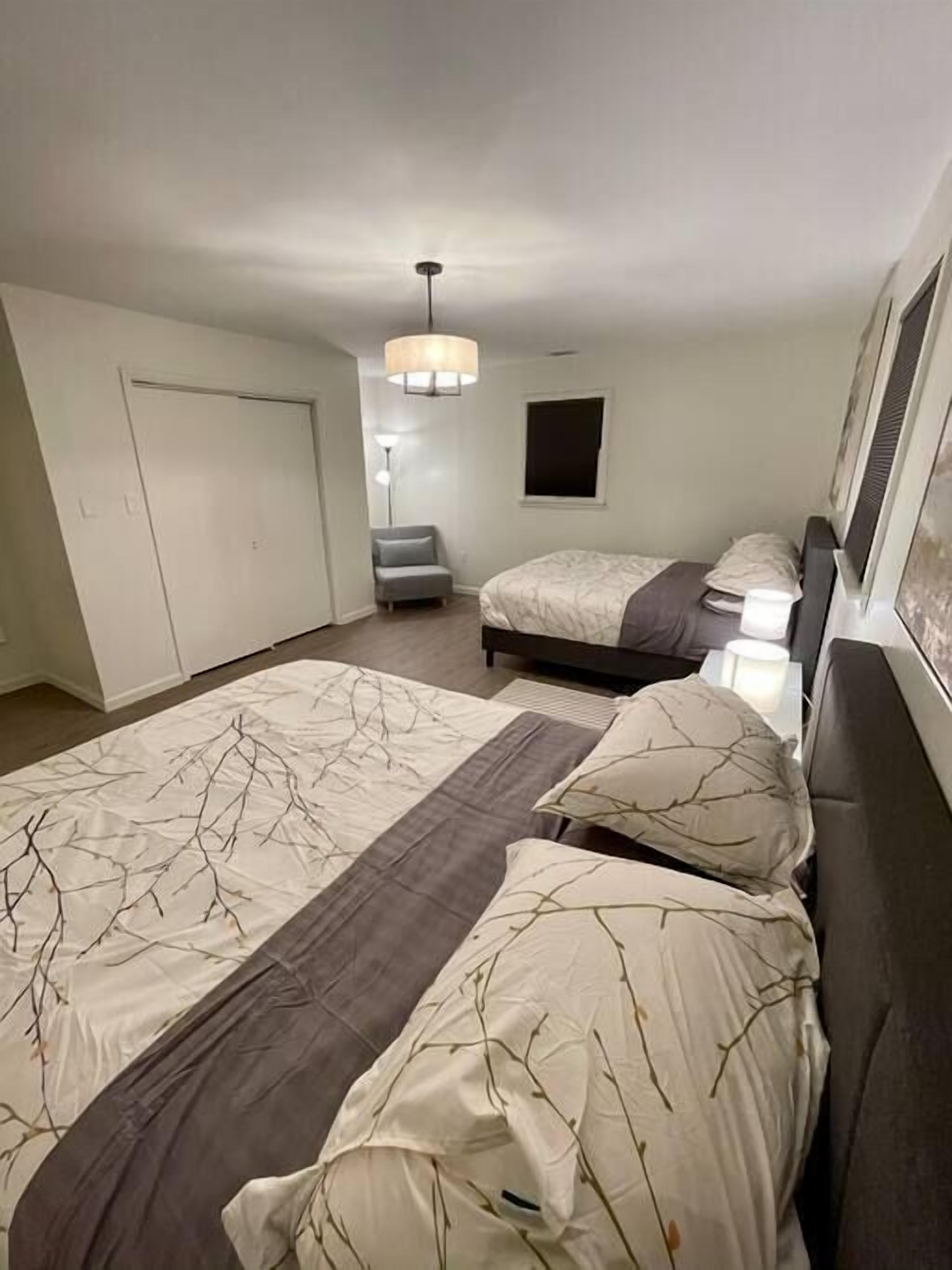 Une chambre à coucher comprenant un grand lit, un plus petit lit, une chaise, un bureau et un luminaire suspendu.