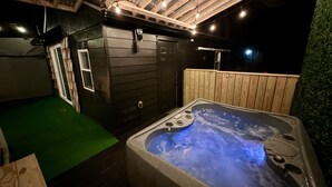 Un jacuzzi con cubierta de madera y zona de césped artificial verde.