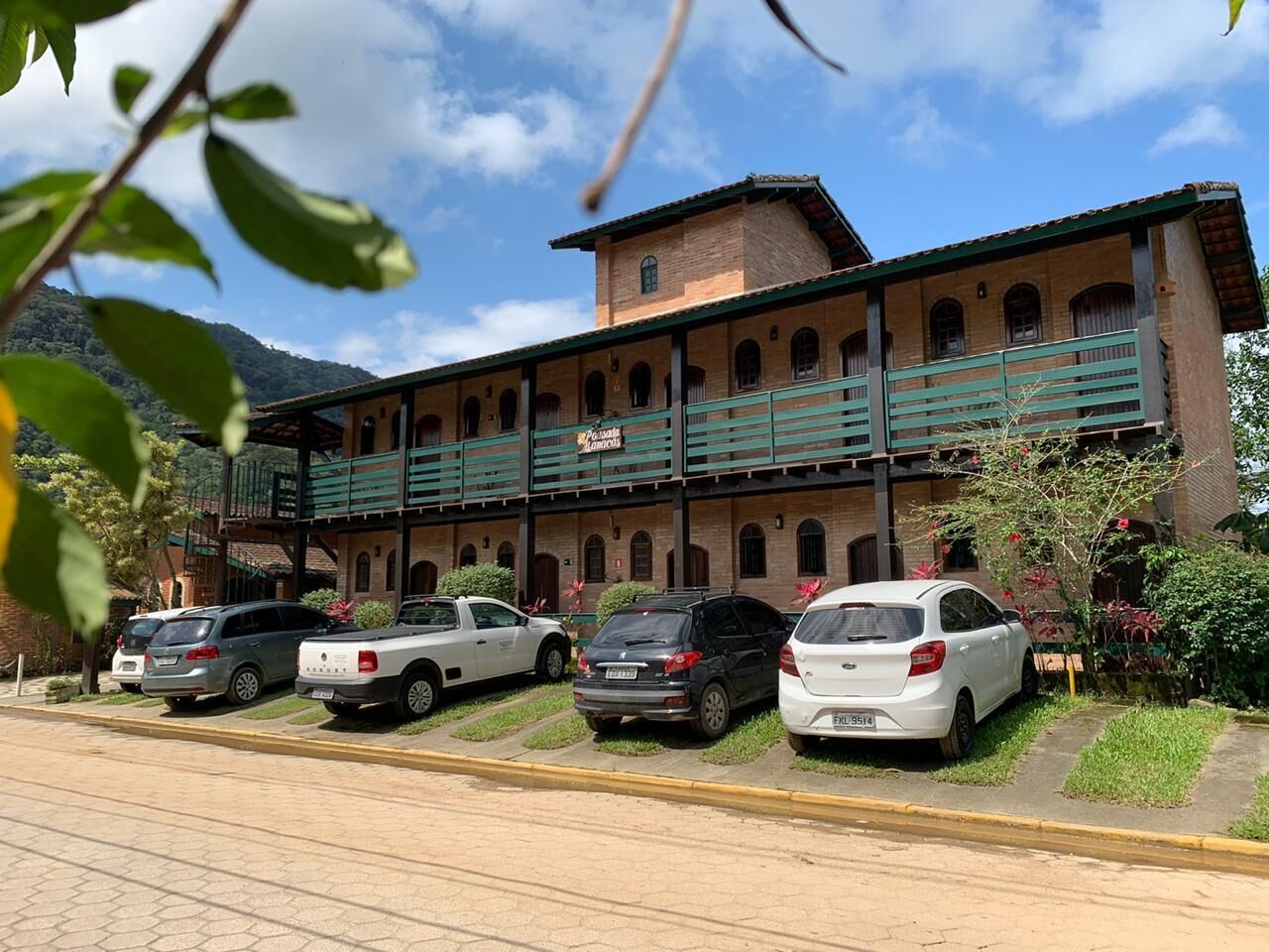 Um edifício com fachada de tijolos, várias janelas e uma varanda verde. Vários carros estão estacionados em frente.