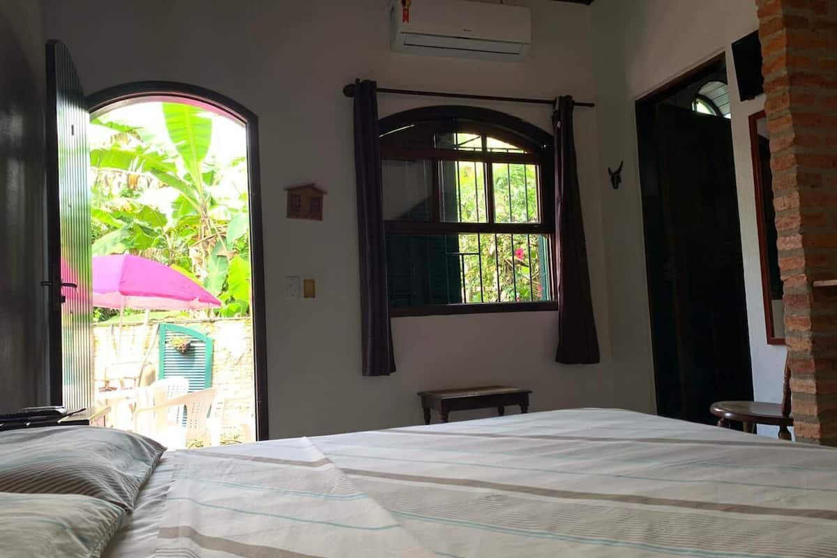 Un dormitorio con cama, ventana, banco y equipo de aire acondicionado.