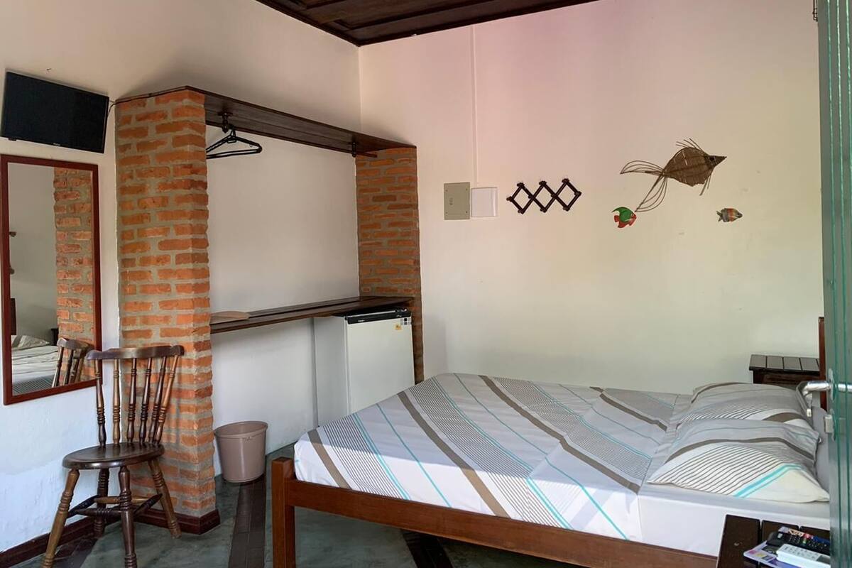 Un dormitorio con cama, escritorio, silla, espejo y un refrigerador pequeño.