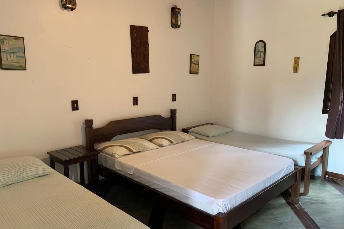 Una habitación con tres camas individuales, cabeceros de madera y una mesita entre las camas.