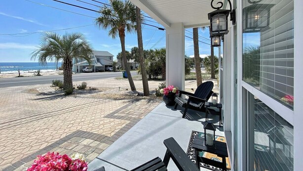 A covered patio with a view of the beach, palm trees, and a parked car. - Swell Life | Walk to Beach | Large Pool | Near 30A & Pier Park | Sleeps 12 (Panama City Beach)