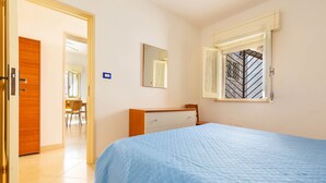 Quarto com cama, cômoda, espelho e janela com grades.