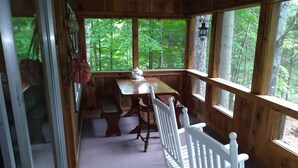 A wooden cabin with a dining area, a rocking chair, and large windows overlooking a forest. - Private lakeside cabin for those looking for peace and quiet in Brant Lake. (Brant Lake)