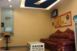 A reception area with a computer monitor, a sofa, and a television mounted on the wall.