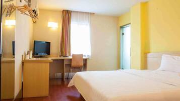 A hotel room with a bed, a desk with a chair, a television, and a window with curtains.