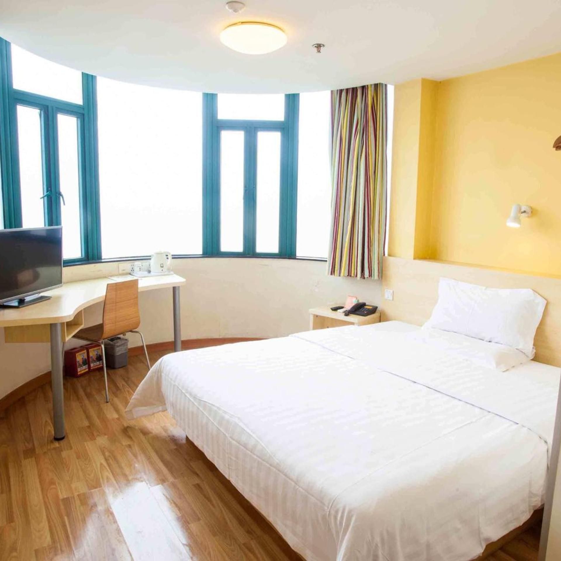 A hotel room with a bed, desk, chair, television, and a window with curtains.