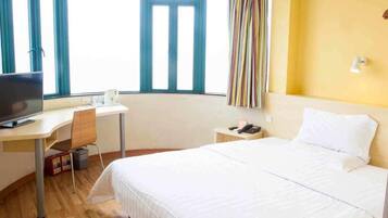 A hotel room with a bed, desk, chair, television, and a window with curtains.
