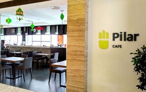 A restaurant interior with tables and chairs, a counter, and a wall with the 'Pilar Cafe' sign.