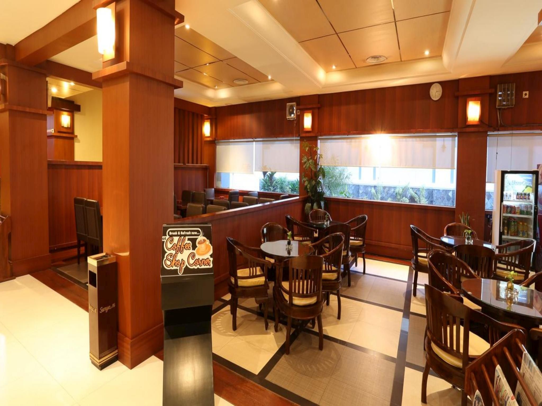 A hotel lobby with wooden paneling, a coffee shop corner, and a seating area with tables and chairs.