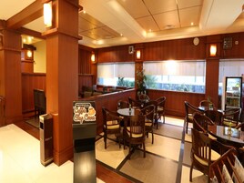 Un vestíbulo de hotel con paneles de madera, una zona de cafetería y un área de descanso con mesas y sillas.