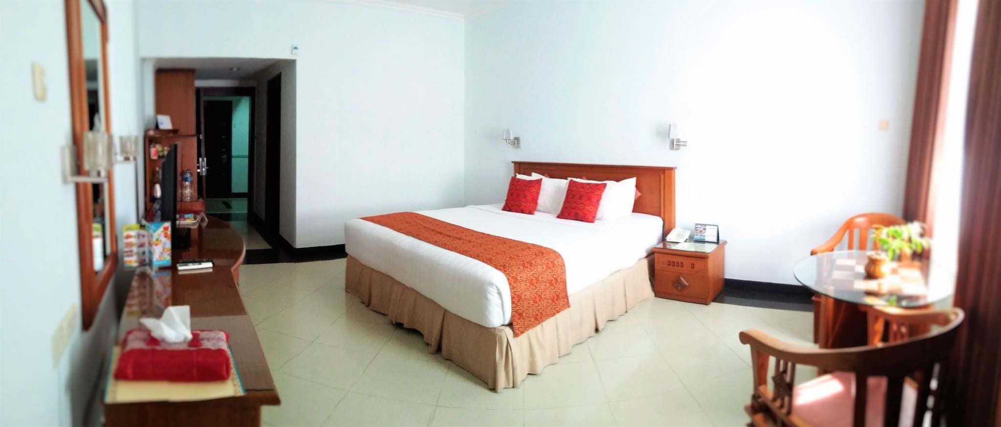 A hotel room with a bed, bedside table, chair, and a desk with a chair.