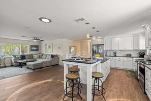 A modern kitchen with white cabinets, a central island with stools, and a dining area with a sofa and coffee table.