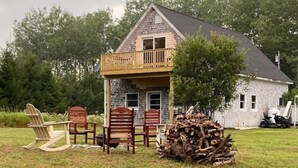 A stone house with a balcony, a pile of firewood, and outdoor furniture. - The Acadia Gateway House (Trenton)