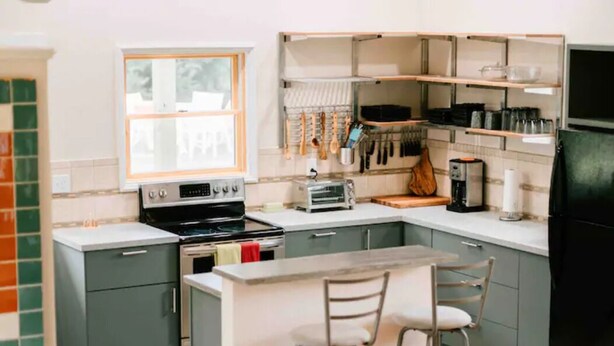 A compact kitchen with a central island, a stove, a toaster, and hanging utensils. - The Acadia Gateway House (Trenton)