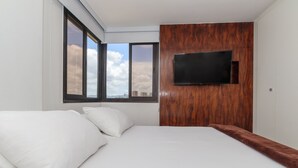 Ein modernes Hotelzimmer mit einem großen Bett, einem an einer Holzwand montierten Fernseher und Blick auf die Stadt durch große Fenster.