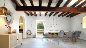 Een eetruimte met een houten plafond, witte muren en een grote tafel met stoelen. Er staat een kast met decoratieve items en er hangt een spiegel aan de muur.