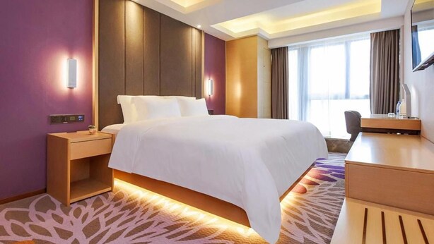 A hotel room with a large bed, bedside tables, a desk, a chair, and a television. - Lavande Hotel (Chongqing)