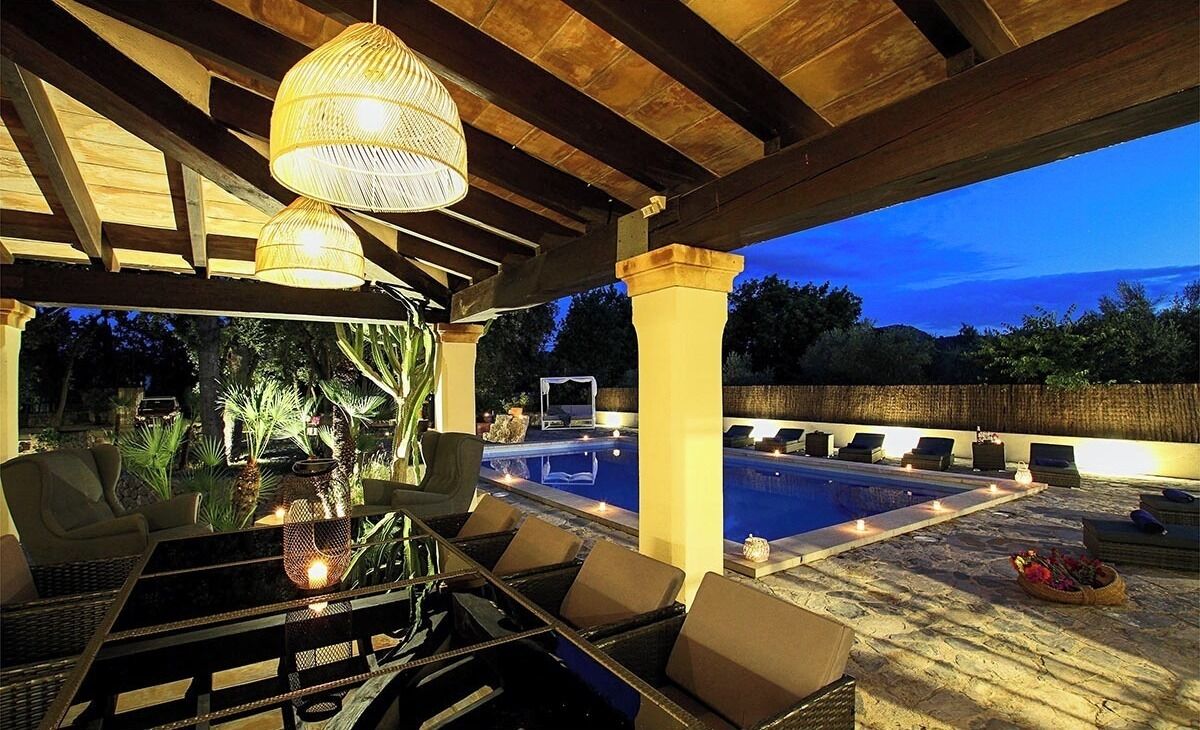 An outdoor lounge area with a pool, wicker furniture, and hanging lights.