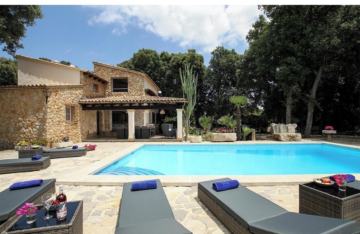 Un espace aménagé au bord de la piscine, avec des chaises longues, un bâtiment en pierre et une piscine à l’eau d’un bleu limpide.
