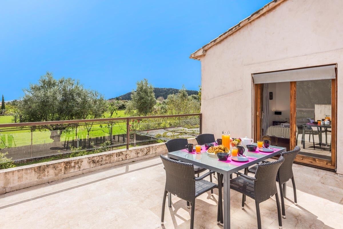 Un balcon avec une table préparée pour le petit-déjeuner, offrant une vue sur un paysage verdoyant et des collines.