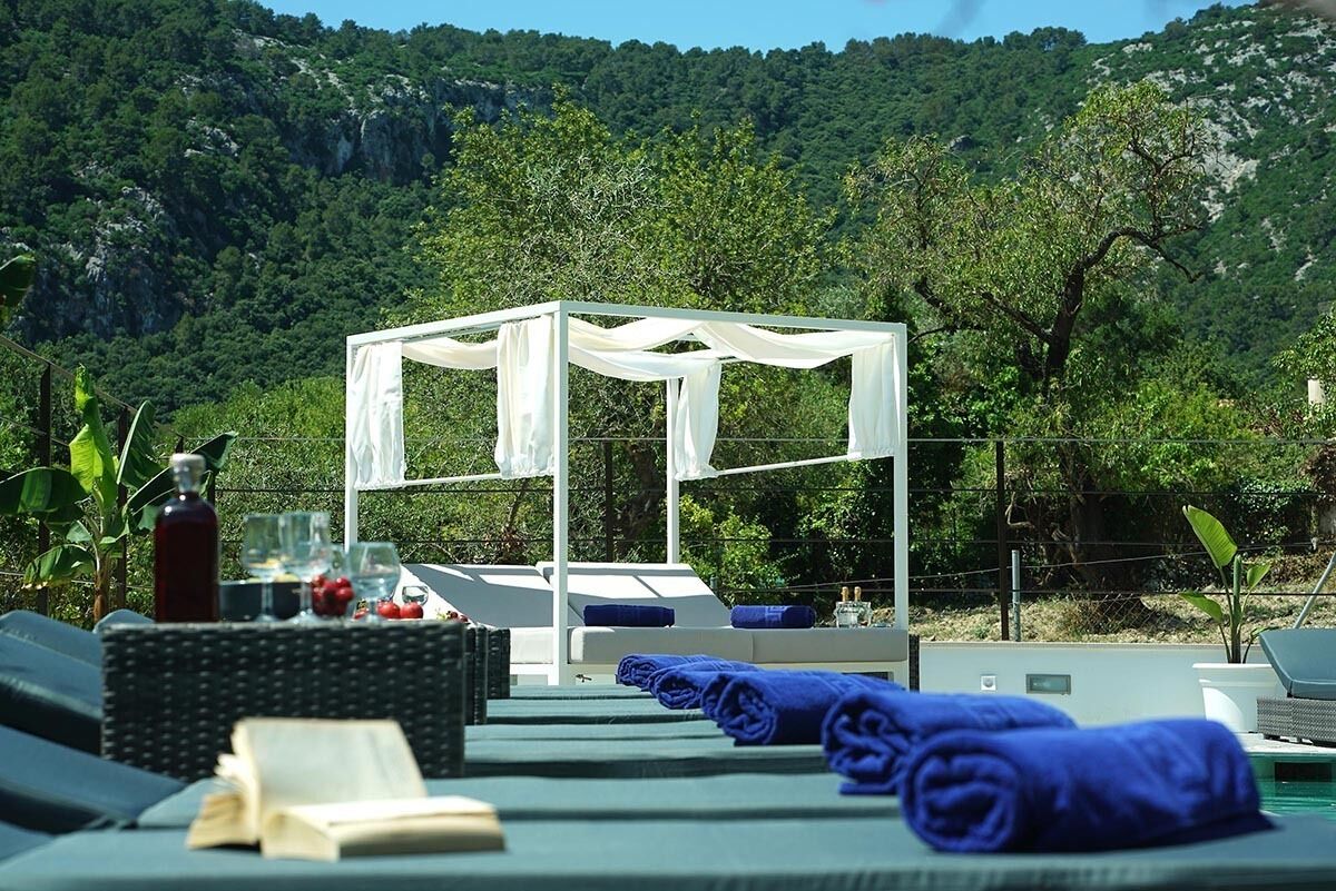 A sunlit outdoor lounge area with a white canopy, lounge chairs, and a table with drinks and snacks.