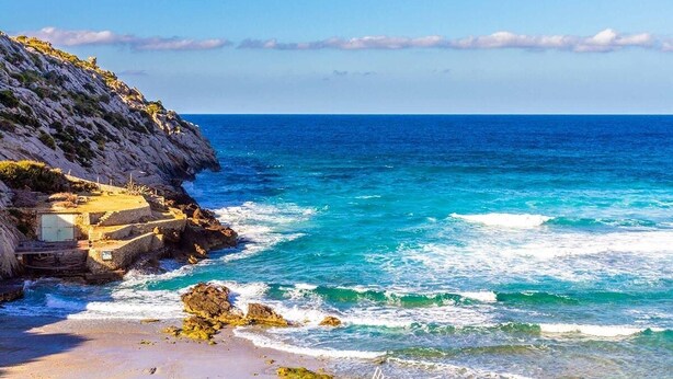 A coastal scene with a rocky cliff and a building with a staircase leading down to the beach. - Villa Cavall, Magnificent house 200 meters from the beach (Cala Sant Vicenç)