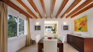 A dining area with a wooden ceiling, a dining table with chairs, a cabinet, and two paintings on the walls.