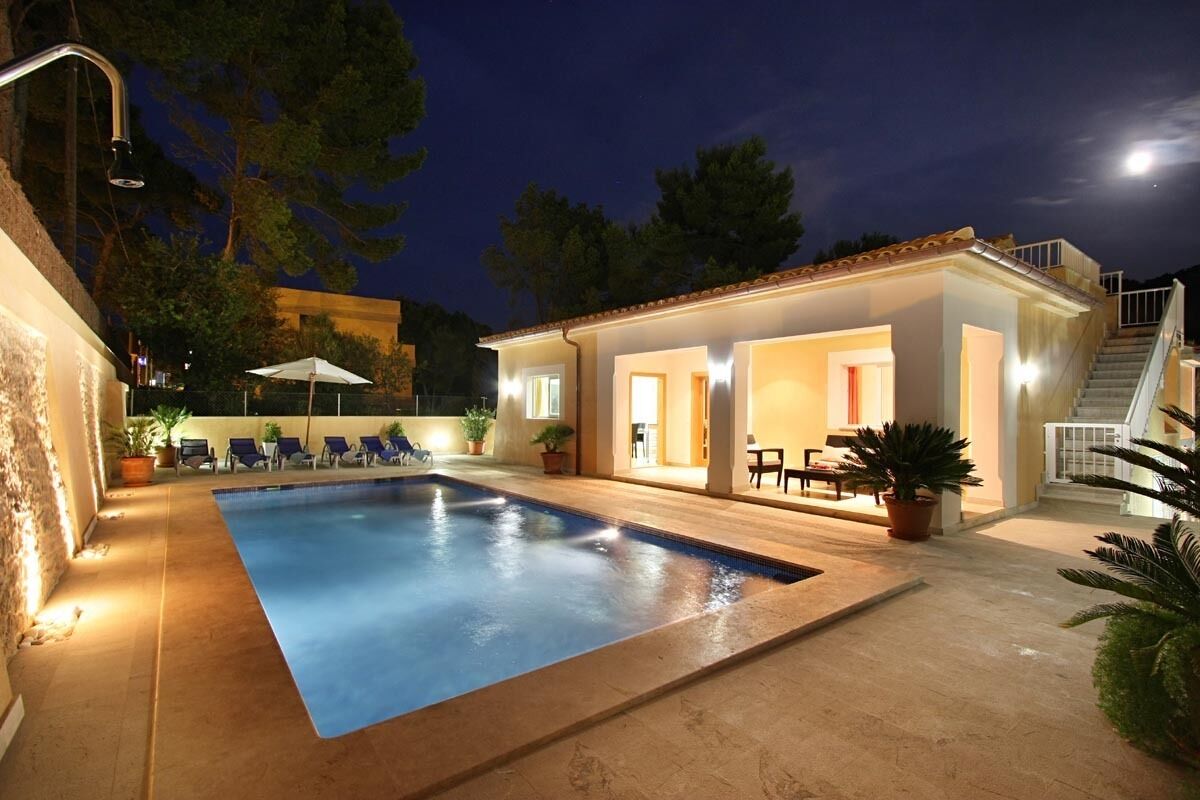 Une piscine avec des chaises longues, un espace salon couvert et un escalier menant à un deuxième étage.
