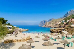 A beach with thatched umbrellas, sun loungers, and a rocky coastline. - Villa Medina, 200m. from the beach (Cala Sant Vicenç)