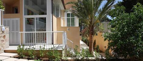 A two-story building with a balcony, a palm tree, and a garden with stepping stones.