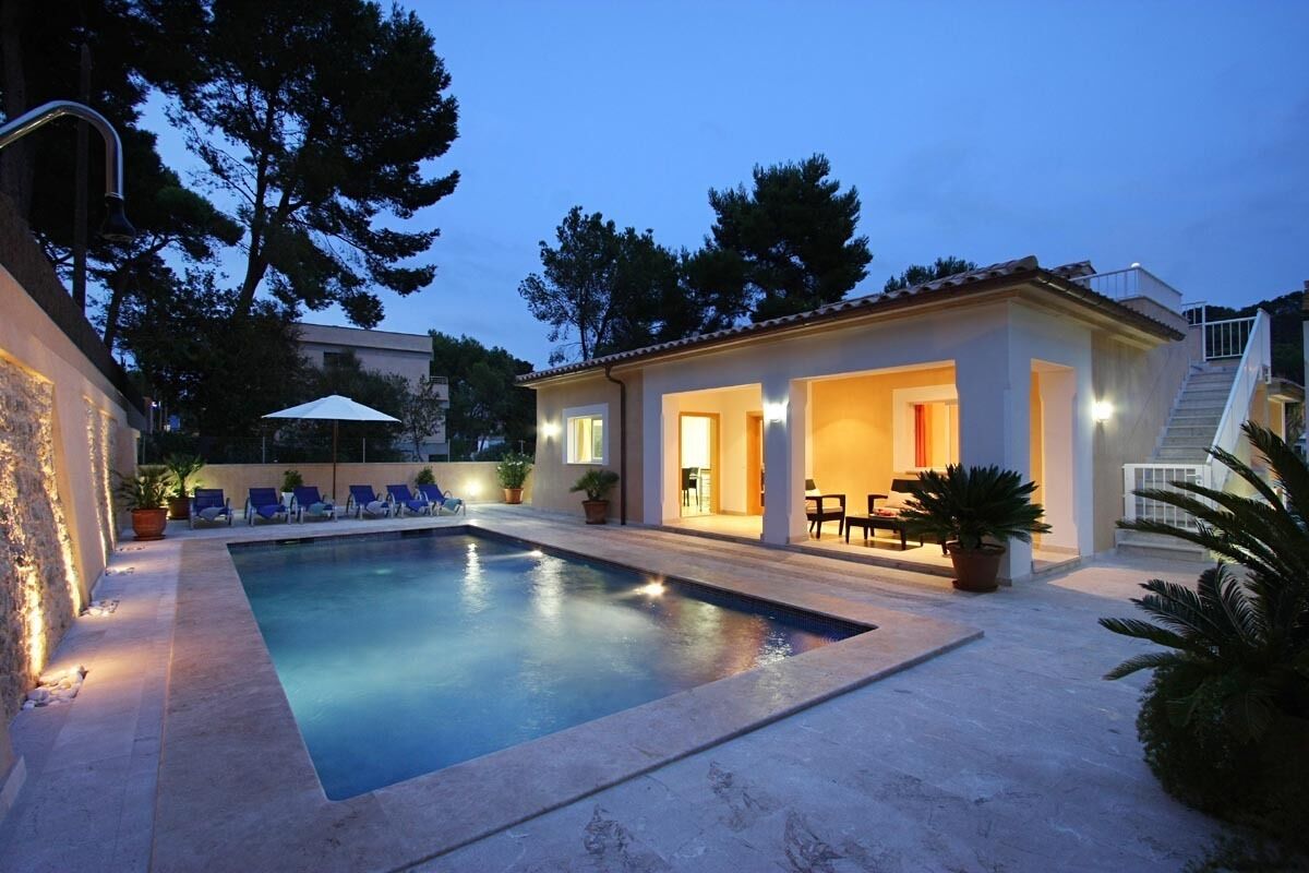 A swimming pool with lounge chairs, a covered patio area, and a staircase leading to a second floor.