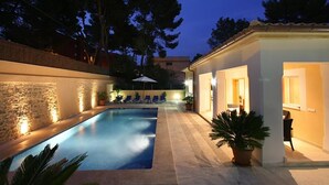A swimming pool with a stone wall on one side and a building with a balcony on the other.