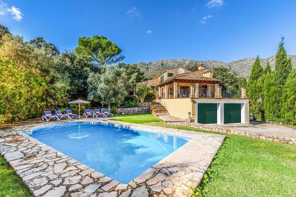 Una piscina con piastrelle di pietra, una casa con tetto in tegole e un garage.