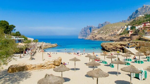 A beach with thatched umbrellas, sun loungers, and a rocky coastline. - Villa Formosa, One of the most loved properties. Impressive garden (Cala Sant Vicenç)