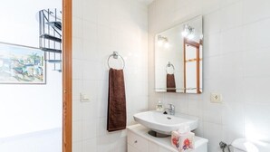 Een badkamer met witte tegels, een wastafel, een spiegel, een handdoekhouder en een toilet.