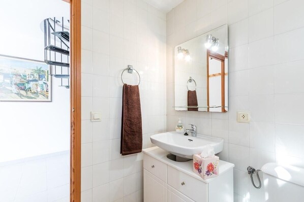 A bathroom with white tiles, a sink, a mirror, a towel ring, and a toilet.