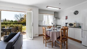 Een moderne keuken met witte kasten, een eettafel met stoelen en een bank in de aangrenzende woonkamer.