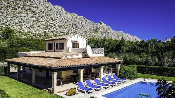 A villa with a swimming pool, lounge chairs, and a mountain backdrop. - Villa Barraca, Peace and relax at 10m. walking to Puerto Pollensa (Port de Pollença)