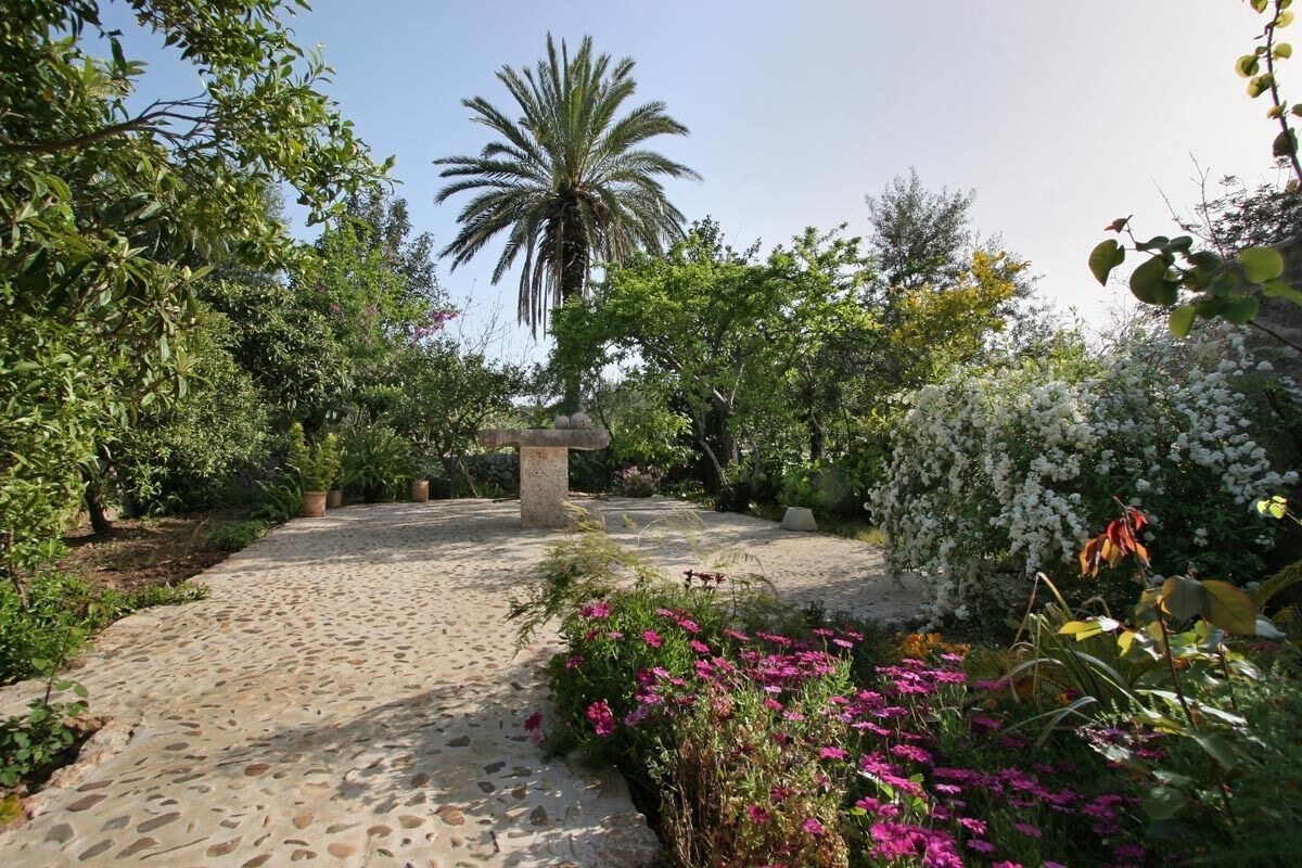 A garden pathway leading to a stone monument surrounded by lush greenery and flowering plants.
