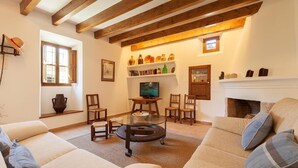 A cozy living room with a fireplace, wooden beams, and a television on a stand. - Villa Butxaco, One of the most popular, and for good reason (Pollença)