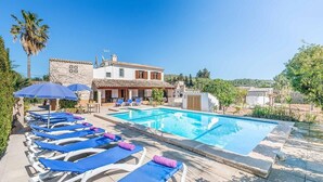 Ein Poolbereich mit Liegestühlen und Sonnenschirmen, ein Schwimmbecken und ein Gebäude mit einem Kachel­dach.