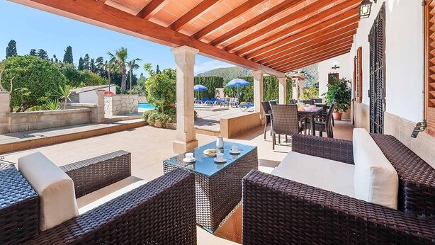 Ein Terrassenbereich im Freien mit Korbmöbeln, einem Pool und einem überdachten Bereich mit Sonnenschirmen.