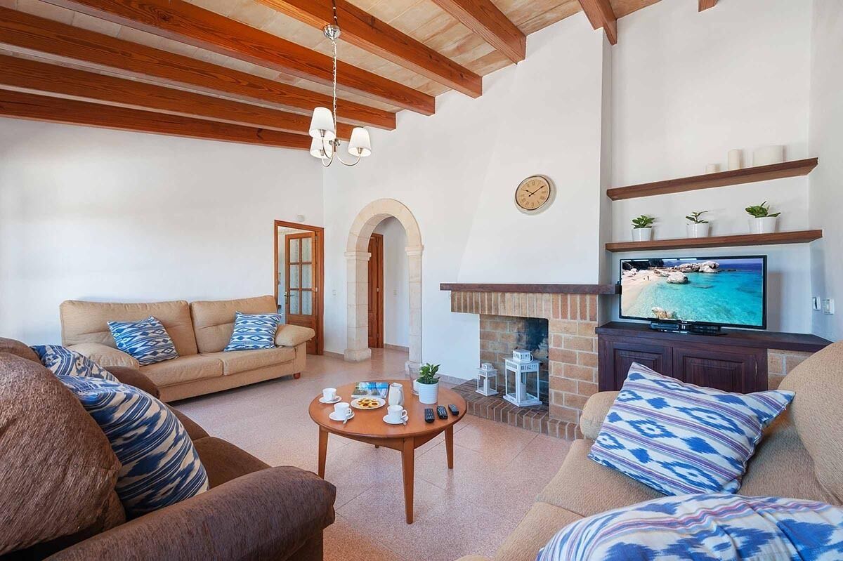 Una sala de estar con sofá, sillones, una mesa de centro con alimentos para el desayuno, chimenea y televisor que muestra una escena de playa.