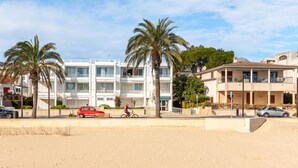 A beachfront hotel with multiple floors, palm trees, and a sandy beach. - Sivella Apartament, Front-line studio located in Puerto Pollensa (Port de Pollença)