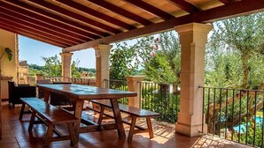 A covered outdoor patio with a wooden table and benches, surrounded by columns and a railing. - Villa Hostalet,  Spaciousness and nature near the golf course (Pollença)