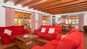 A living room with red sofas, wooden beams, large windows, and a dining area. - Villa Hostalet,  Spaciousness and nature near the golf course (Pollença)